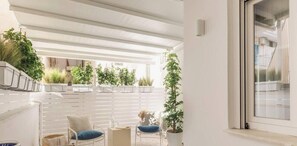 Een modern interieur met een wit plafond, een witte muur en een raam. Er staan potplanten en er is een stoel met een kussen.