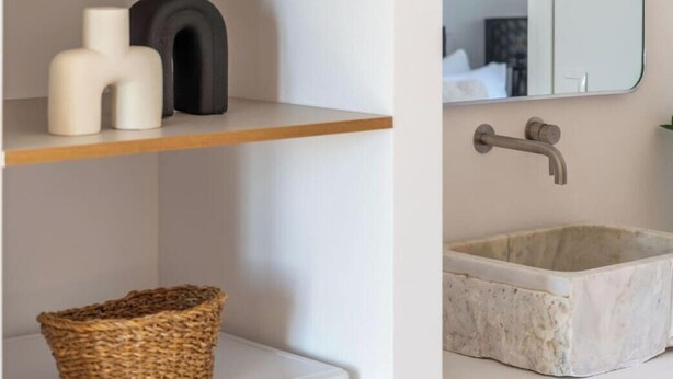 Un bagno con un lavandino bianco, uno specchio e uno scaffale con oggetti decorativi.