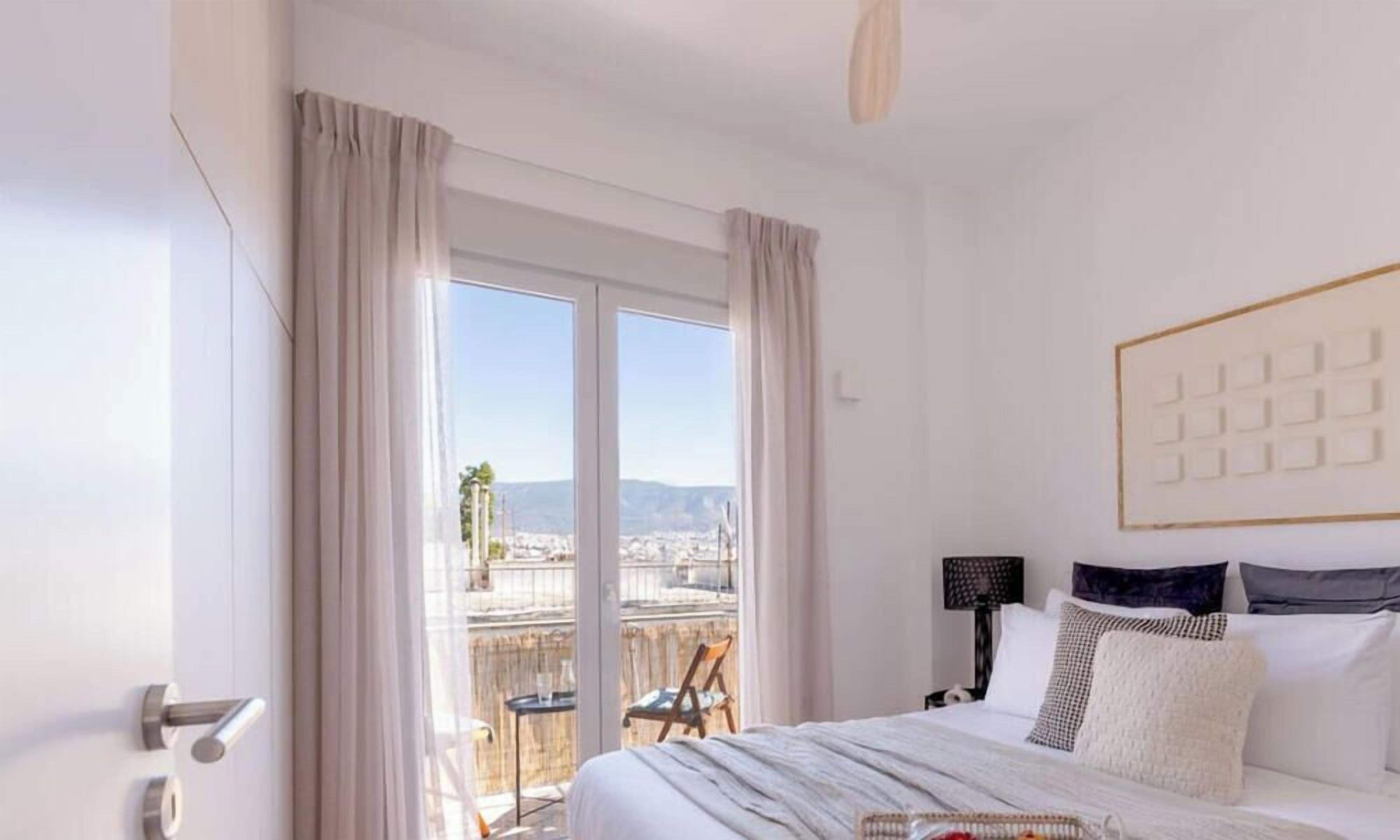 A hotel room with a bed, a view through a large window, a chair, and a table.