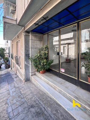 A building with a blue awning, a potted plant on the steps, and a sign on the door. - Acropolis Hillside Escape Fireplace & Sea Views (Athina)