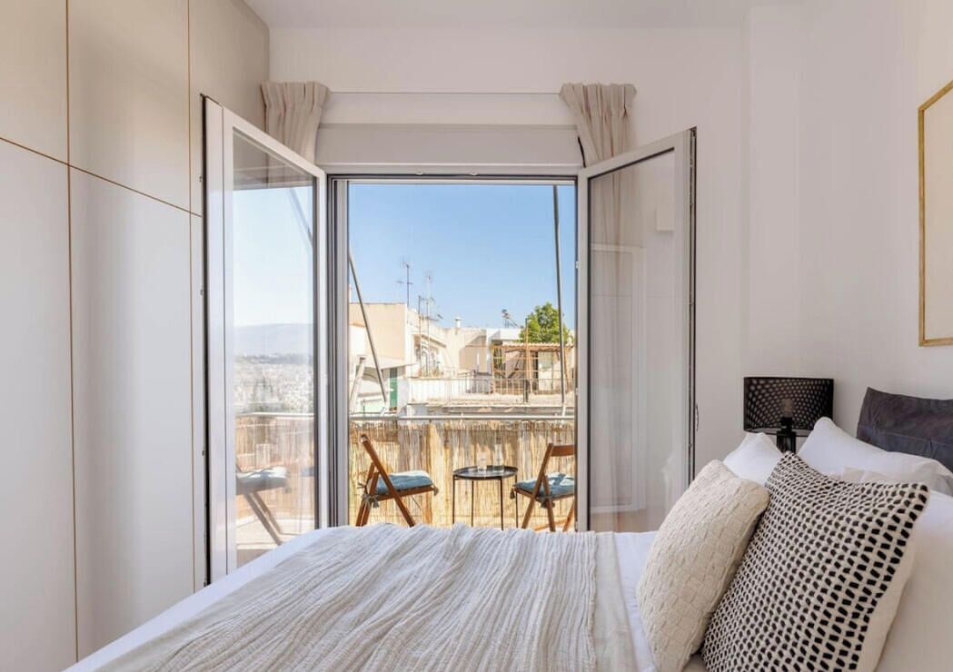 A bedroom with a large bed, a nightstand, a chair, and a view through a sliding glass door to an outdoor balcony.