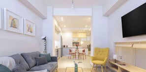 A modern living room with a sofa, a yellow armchair, a coffee table, and a flat-screen TV mounted on the wall. - Cozy Hub - Work, Relax, Explore - Prime Location (Athina)