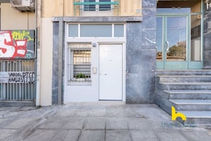 A building entrance with a white door, a metal gate with graffiti, and a staircase leading up to a balcony. - Cozy Hub - Work, Relax, Explore - Prime Location (Athina)