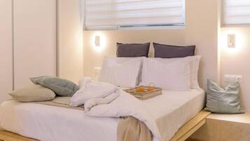 Una cama bien hecha con sábanas blancas, una cesta de naranjas y algunos almohadones.