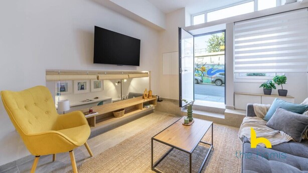 A modern living room with a flat-screen TV mounted on the wall, a yellow armchair, a grey sofa, and a coffee table. - Cozy Hub - Work, Relax, Explore - Prime Location (Athina)