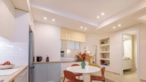 A modern kitchen with white cabinets, a round dining table, and a vase of flowers. - Cozy Hub - Work, Relax, Explore - Prime Location (Athina)