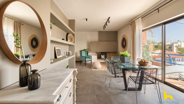 Et moderne spiseområde med et glasbord, metalstole og udsigt over byen gennem store vinduer.