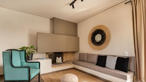 En moderne stue med sofa, en turkis lænestol, pejs og et dekorativt vægkunstværk.