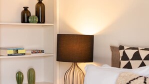 Et pænt opredt soveværelse med seng, natbord med lampe, bogreol og dekorative puder.