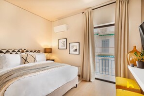 Une chambre d’hôtel avec un lit, une table de chevet avec une lampe, une plante en pot et une vue sur un balcon.