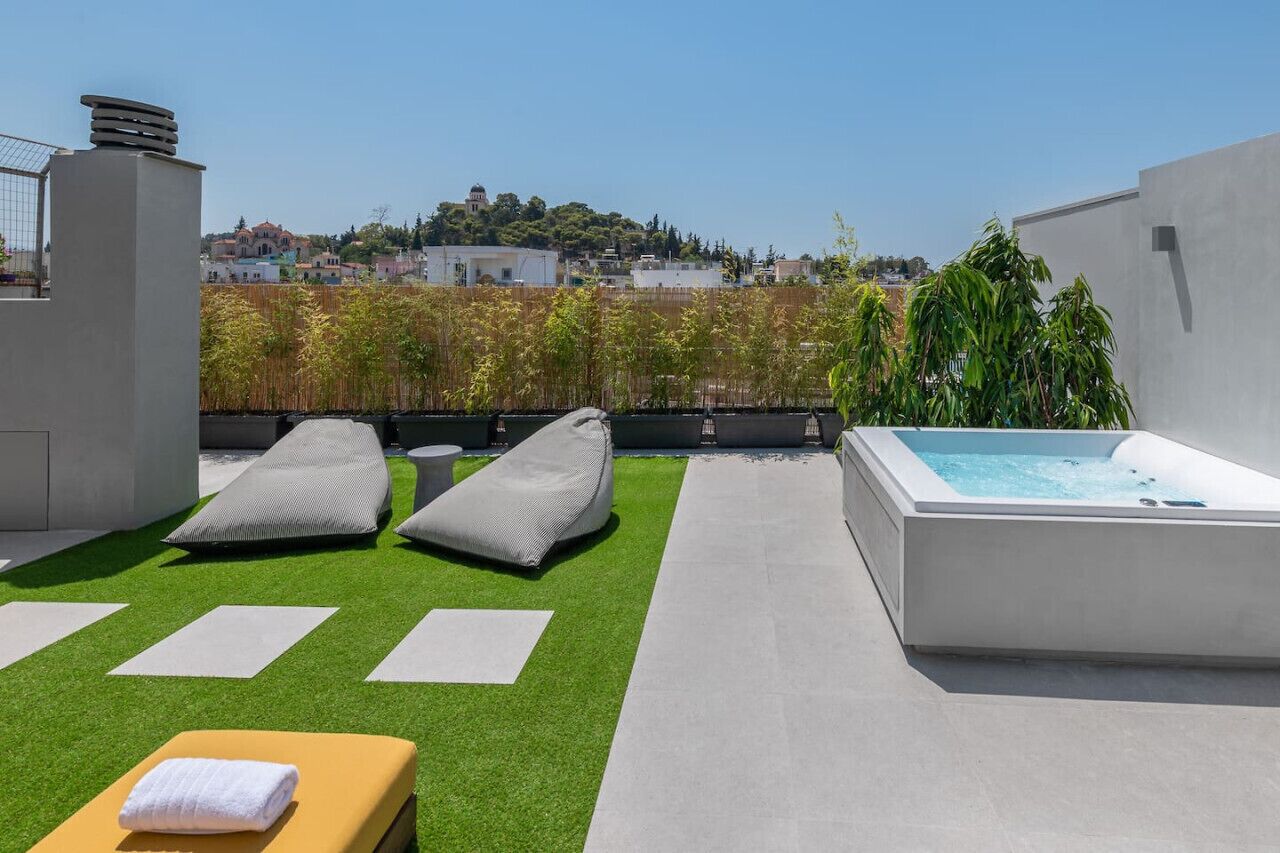Een terras op het dak met een jacuzzi, lounge stoelen en uitzicht op een heuvelstad.