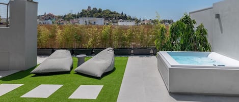 Una terraza en la azotea con jacuzzi, sillas de descanso y vistas a un pueblo en la ladera.