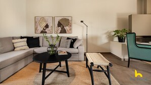 En moderne stue med en grå sofa, et sort sofabord, en flettet bænk og to billeder i rammer på væggen.