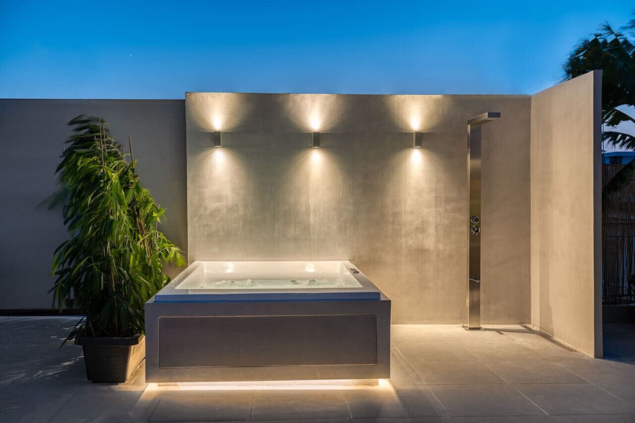 A modern outdoor spa area with a rectangular hot tub, a shower, and a potted plant.