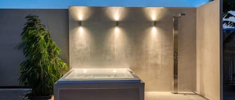 A modern outdoor spa area with a rectangular hot tub, a shower, and a potted plant.