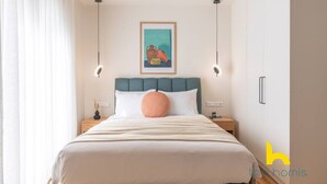 Una habitació ben ordenada amb un llit, una taula de nit, una finestra amb cortines i una obra d'art penjada a la paret.