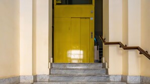 Una escalera de mármol que conduce a una puerta amarilla, con barandilla a la derecha.