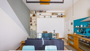 Una cocina moderna con horno empotrado, una zona de comedor con mesa y sillas, y una estantería llena de libros y objetos decorativos.