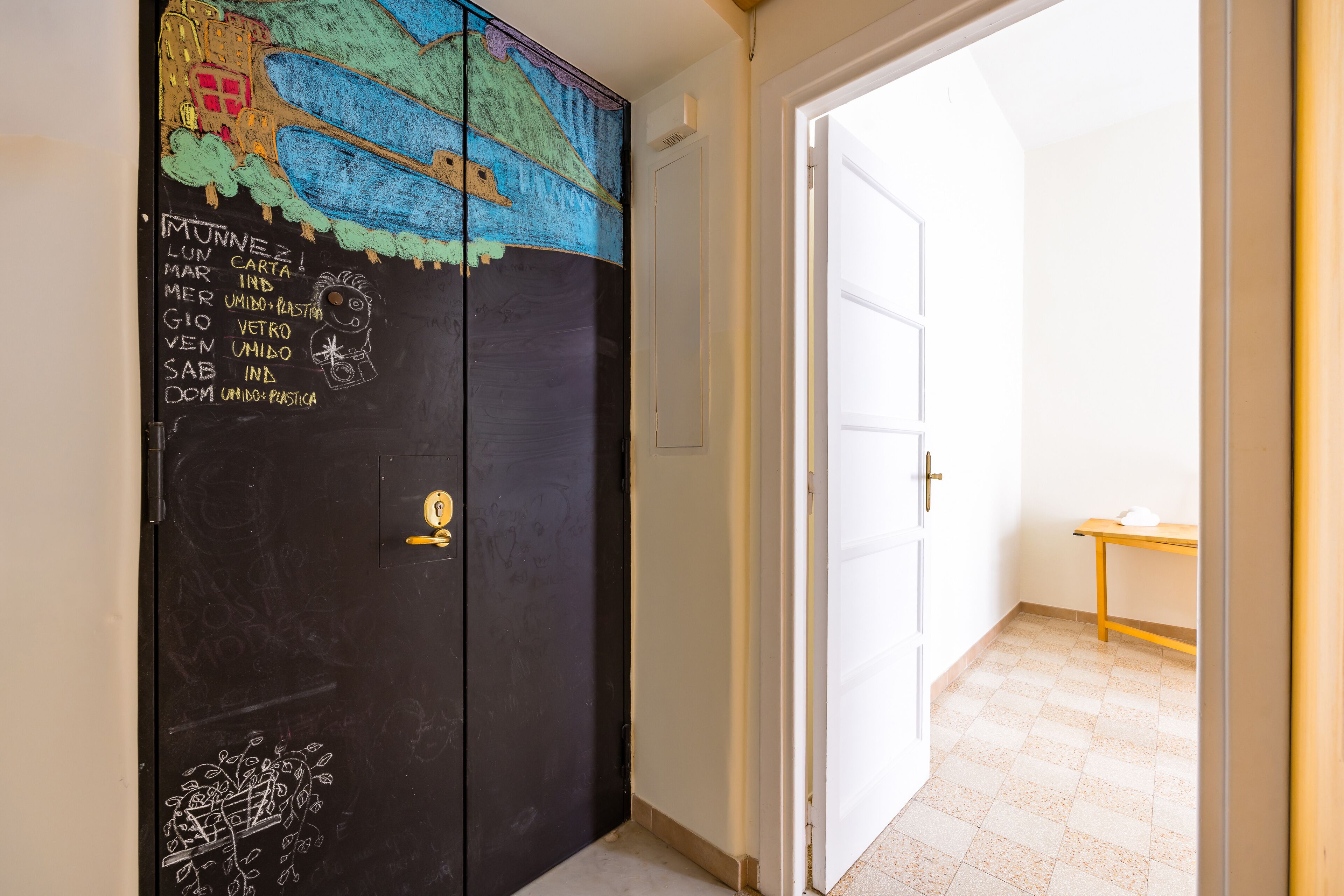 Un corridoio con una porta nera decorata da graffiti colorati e un piccolo tavolo con una tazza.
