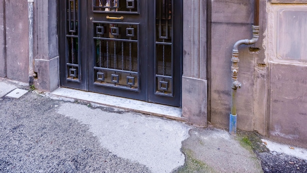 Una entrada de edificio con una puerta negra grande y ornamentada, una pequeña ventana sobre la puerta y el número '12' en la pared.