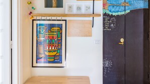 Un pasillo con un banco de madera, un estante con una cesta, un cuadro enmarcado y una puerta con un mural colorido.