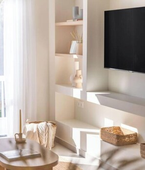 Ein modernes Wohnzimmer mit einem wandmontierten Flachbildfernseher, einem runden Holztisch und einem dekorativen gewebten Korb.