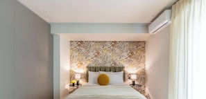 A hotel room with a floral wallpaper headboard, a bed with white bedding, two bedside lamps, and an air conditioning unit.