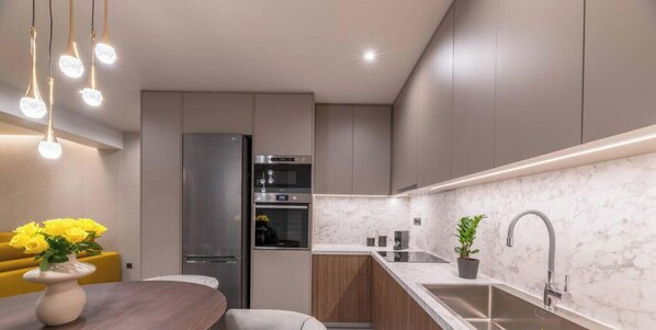 A modern kitchen with a marble countertop, stainless steel appliances, and pendant lighting.