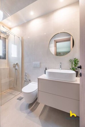 Un baño moderno con ducha envuelta en vidrio, inodoro, lavamanos con espejo y una planta en maceta.