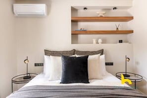 Ein Schlafzimmer mit einem Bett, Nachttischen, einer Wand-Klimaanlage und eingebauten Regalen mit Dekoration.