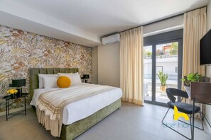 Habitación de hotel con cama, escritorio, silla, televisor y balcón con plantas.