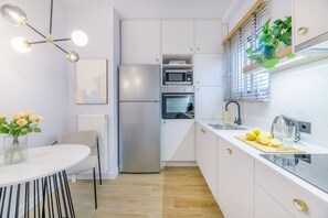 A modern kitchen with white cabinetry, a stainless steel refrigerator, a microwave, and a sink with a cutting board and lemons. - 50 Shades of Athens, Kingsize Suite with Jacuzzi! (Athina)