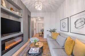 A modern living room with a flat-screen TV, a fireplace, a sofa with cushions, and artwork on the walls. - 50 Shades of Athens, Kingsize suite with Jacuzzi! (Athina)