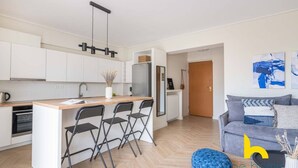 Una cuina moderna amb armaris blancs, una illa central amb tamborets i un refrigerador, i una cafetera.