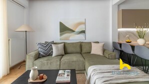 Una sala de estar moderna con un sofá verde, una mesa de centro con un libro y un florero, una lámpara de pie y un cuadro en la pared.