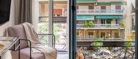 A balcony with a view of a multi-story building, a chair, and a table.