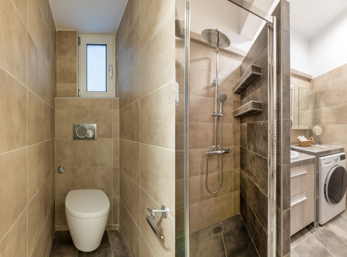 A compact bathroom with a toilet, a shower enclosure, and a washing machine.