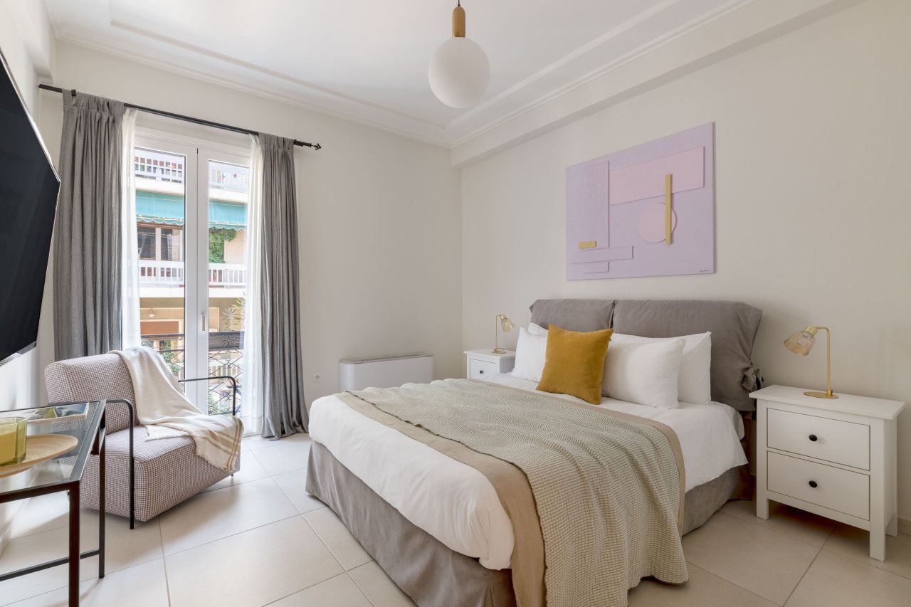 Un dormitorio con una cama, mesitas de noche, una silla y una ventana con cortinas.