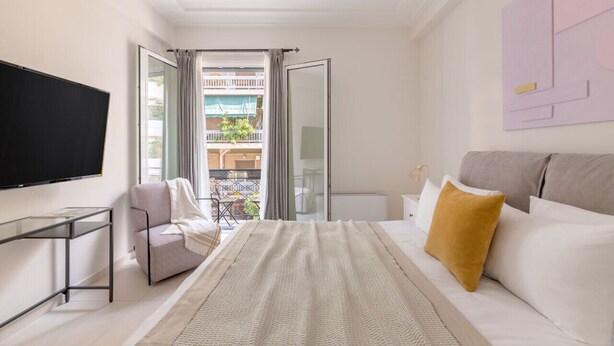 Ett modernt hotellrum med en stor säng, en TV, ett skrivbord och en balkong med utsikt över staden.