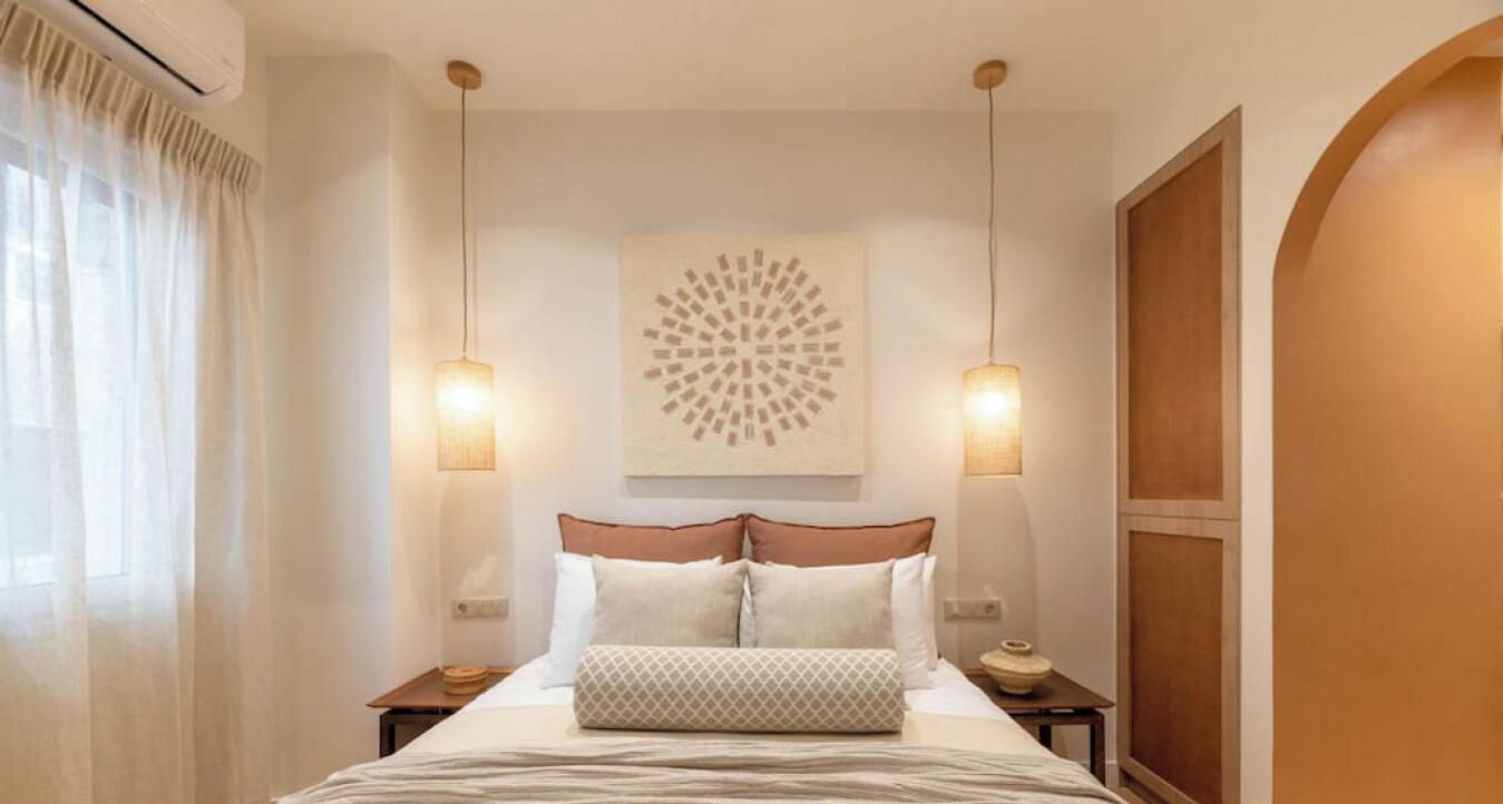 A hotel room with a bed, two bedside tables, a wall-mounted artwork, and a window with curtains.