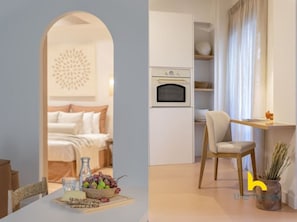 A modern hotel room with a bed, a dining table with a fruit bowl, and a kitchenette with a microwave and oven. - Acropolis Zen Oasis Romantic Retreat in Koukaki! (Athina)