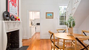 Un comedor con una mesa redonda de madera y cuatro sillas, una chimenea y una cocina al fondo.