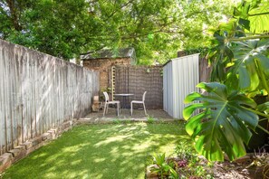 A backyard with a wooden fence, a small brick structure, and a table with chairs. - Stylish 2-Bed House with Private Courtyard (Redfern)