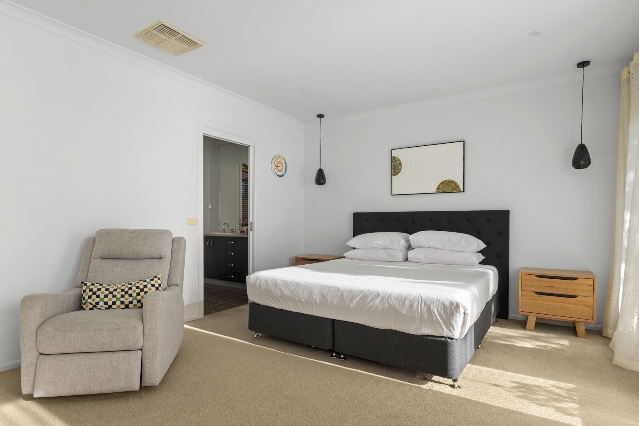 Un dormitorio con una cama, una silla, una mesita de noche y una puerta que da a otra habitación.