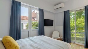 Ein modernes Hotelzimmer mit einem großen Bett, einem Sessel, einem Flachbildfernseher und einer Glastür zum Außenbereich.