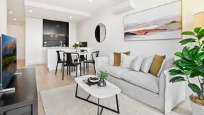 A modern living room with a sofa, coffee table, and a TV. There is a kitchen area with a dining table and chairs. - South Yarra Stay with Balcony Views (South Yarra)