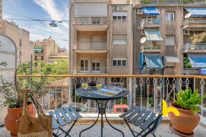 Un balcon avec une table et des chaises, des plantes en pot et une vue sur un immeuble à plusieurs étages.