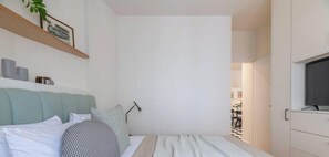 Une chambre à coucher comprenant un lit, une table de chevet, une lampe, un téléviseur et une armoire.