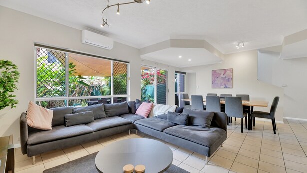 A modern living room with a sectional sofa, a round coffee table, and a dining area with chairs and a table. - Tranquil 3-Bed Unit with Lush Garden Views (Taringa)