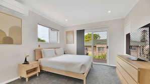 A modern bedroom with a bed, bedside table, and a dresser. There is a window with a view of the outside. - Tranquil 3-Bed Unit with Lush Garden Views (Taringa)